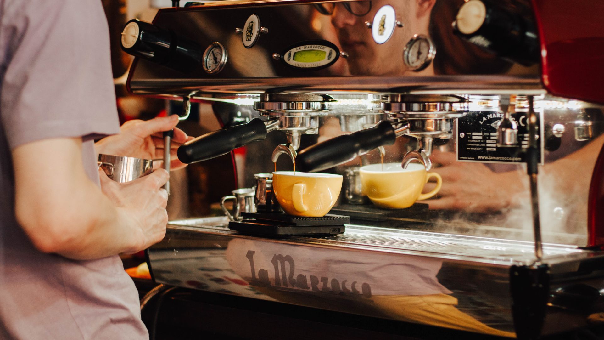 Barista expertly preparing a latte using professional-grade espresso machine in a comfy coffee shop.