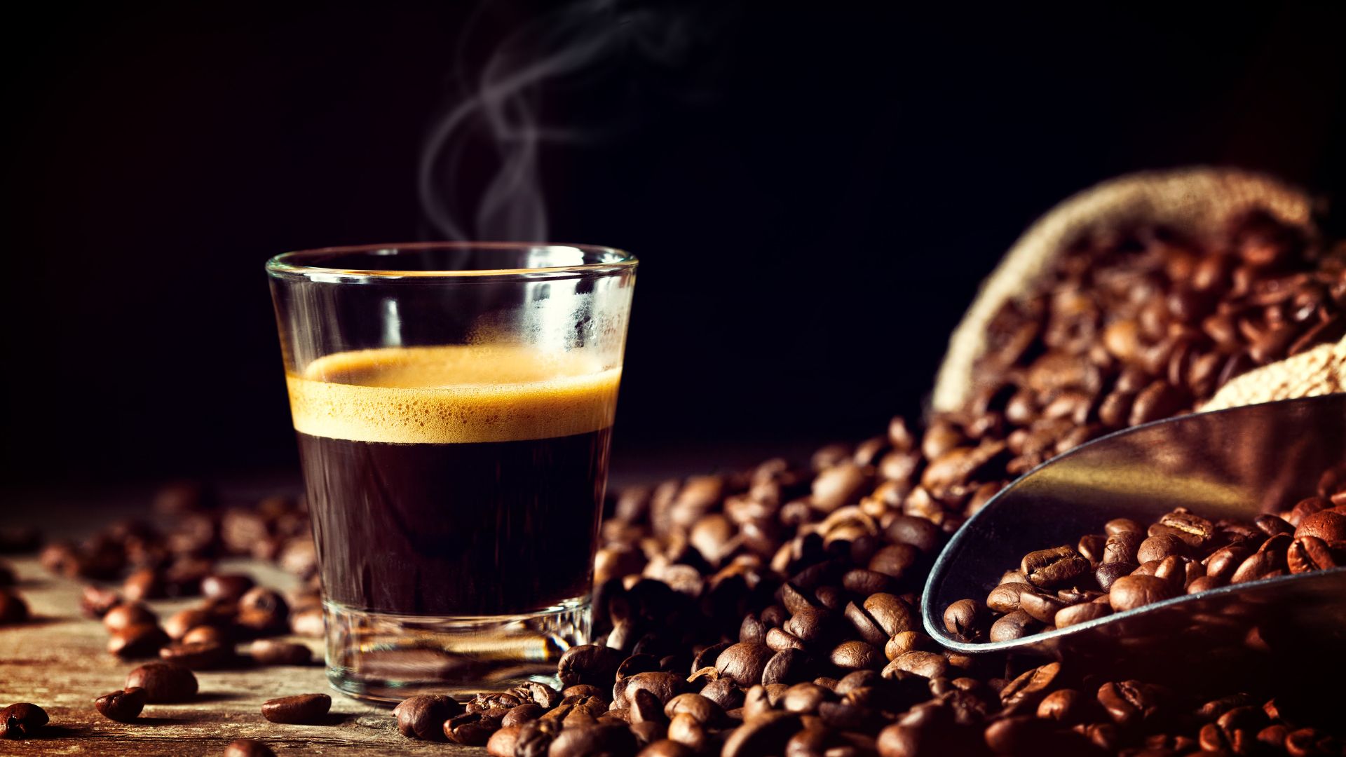 Freshly brewed espresso in glass cup surrounded by aromatic beans and rustic burlap sack.