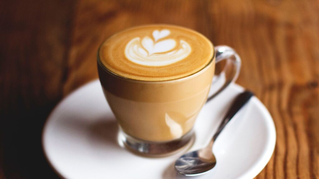 Cortado vs Cappuccino showdown featuring heart latte art design in a clear glass cup on a rustic tabletop.